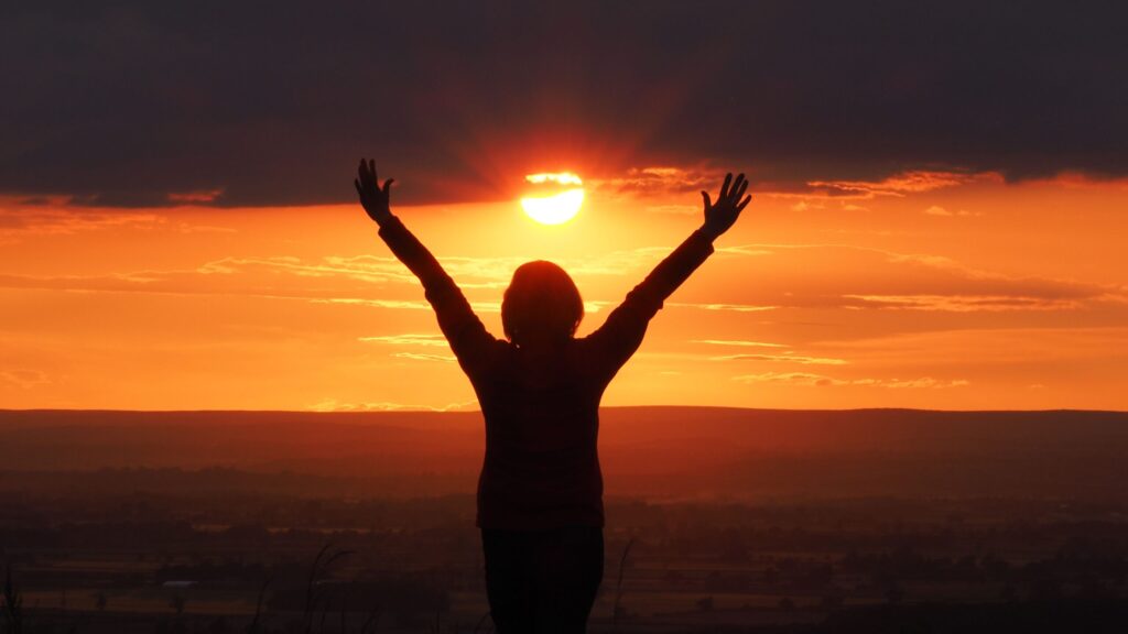 Silhouette of a woman with arms raised against a vibrant sunset in Knapton, England.