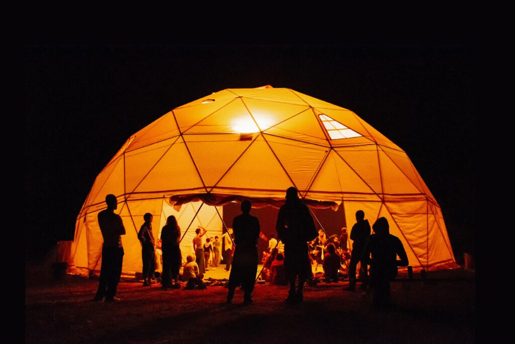 A nighttime gathering with people silhouetted against a glowing geodesic dome.
