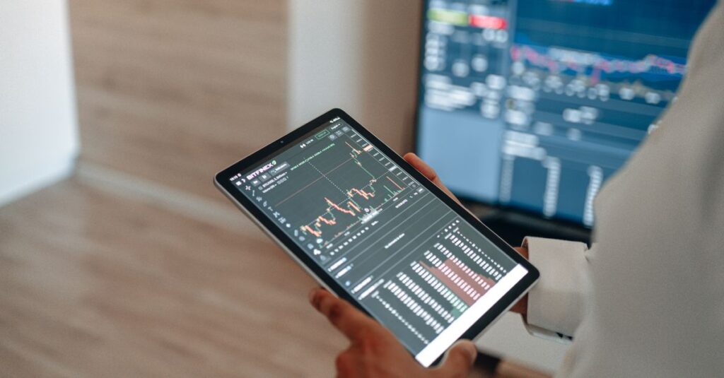 A person uses a tablet to monitor stock market trends and real-time trading graphs.