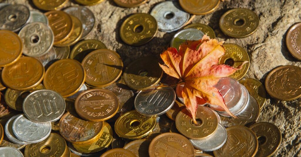 The Yen Carry Trade: A Ticking Clock High angle of various golden and silver coins scattered on rough stone surface with small red leaf in sunny day in fall