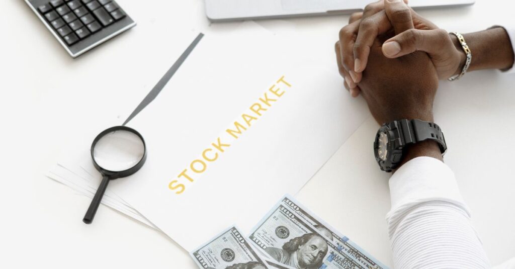 Hands folded over stock market documents with calculator and cash on desk.