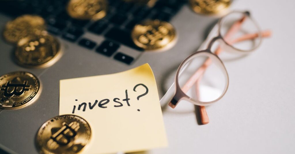 Owning a Slice of Everything: How Blockchain Could Open the Doors Once Reserved for the Rich A close-up of bitcoin coins on a laptop with eyeglasses and a sticky note reading 'invest?'