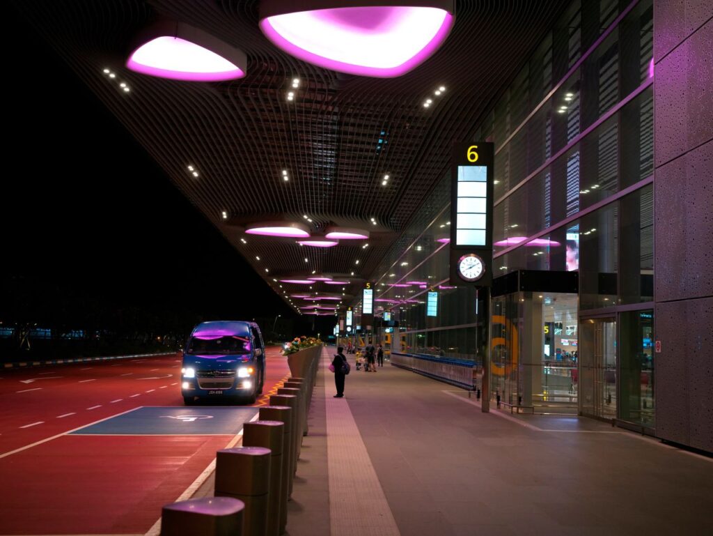 Ten Pounds to Say Goodbye Night view of Singapore's Changi Airport entrance with illuminated canopy and bus.