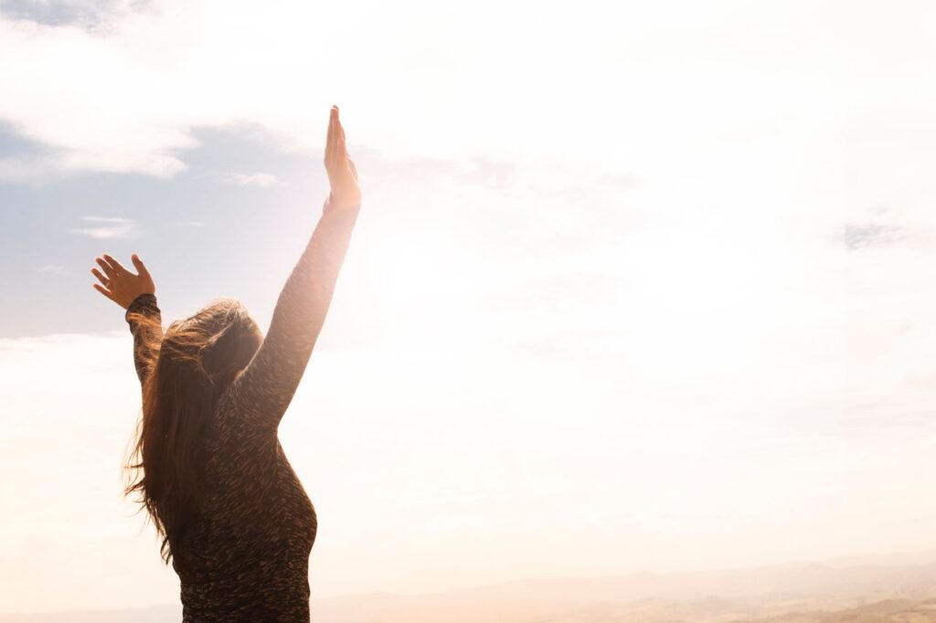 What Enough Looks Like From Here A woman with raised arms enjoying the bright open sky in a serene outdoor setting.