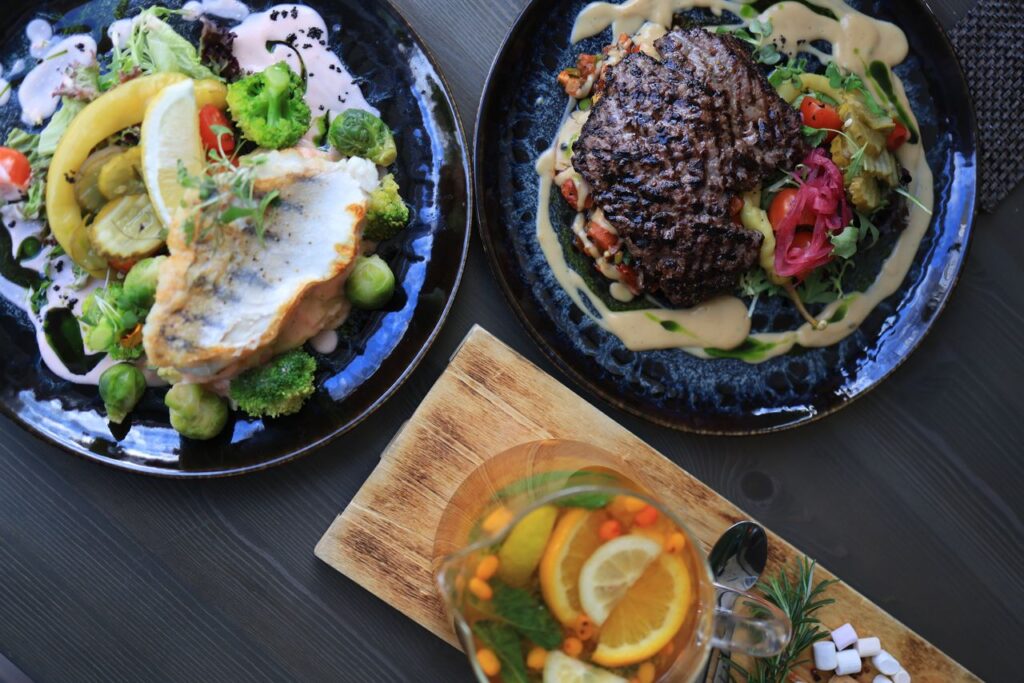 The Table Is Where the Life Actually Happens Top view of gourmet fish and steak dishes with fresh citrus and herbs on a stylish table setting.