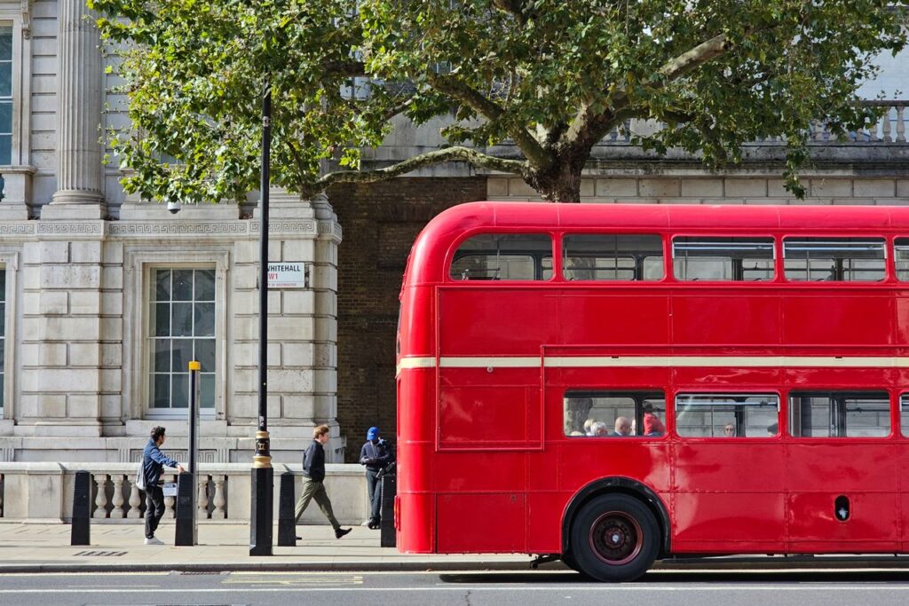 Two Pounds a Journey, and What You Do With It A red double-decker bus on a vibrant London street, capturing urban life.