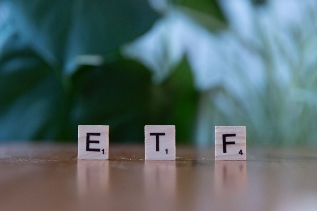 Your "Safe" Index Fund Is a Bet You Never Placed Scrabble tiles spelling ETF on a wooden surface with blurred green background.