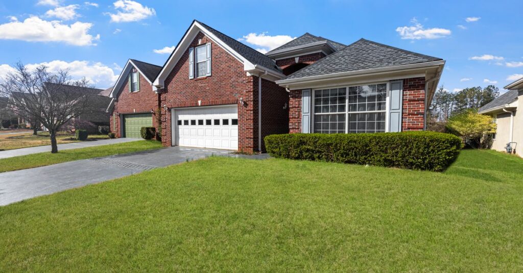 You Can Now Buy a House With Bitcoin. Should You? Lovely red brick suburban house with a well-maintained lawn under a bright blue sky.