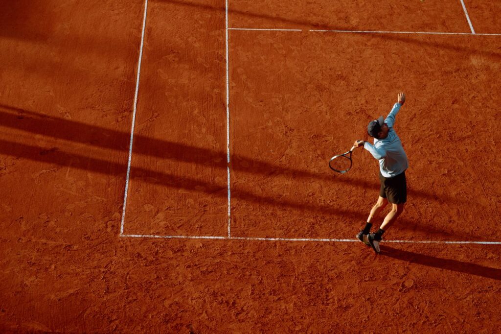 A dynamic shot of a tennis player serving on a clay court during sunset.