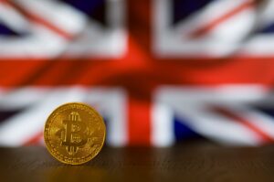 News Close-up of a Bitcoin coin standing against a blurred British flag, symbolizing cryptocurrency in the UK.
