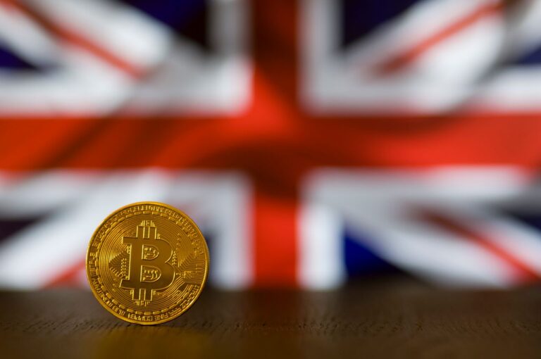 Close-up of a Bitcoin coin standing against a blurred British flag, symbolizing cryptocurrency in the UK.