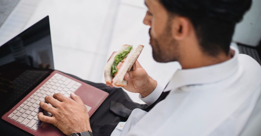 The Long Lunch Is a Power Move A businessman works on his laptop while enjoying a sandwich at an indoor location.