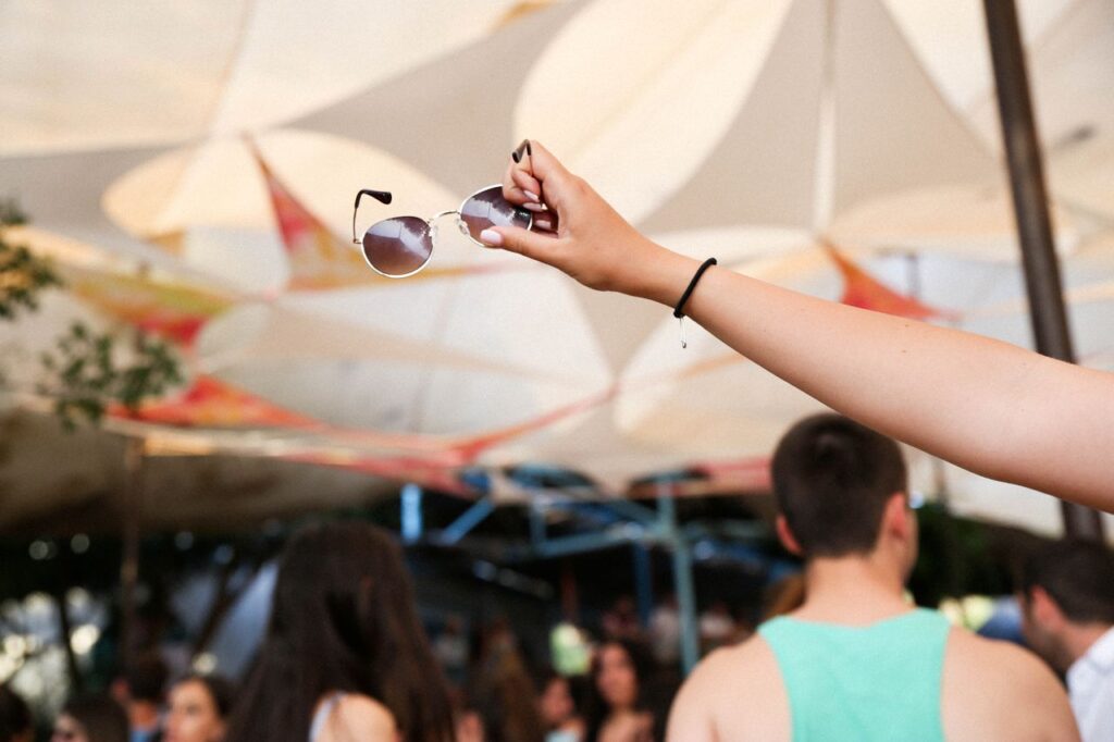 Stylish sunglasses held up at a vibrant summer festival under an art canopy.