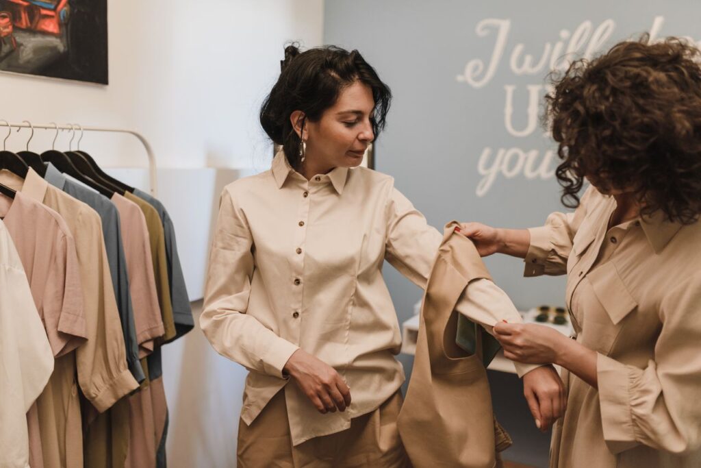 Buy Less, Choose Well Two women shopping in a boutique, examining a shirt together amidst a stylish clothing selection.