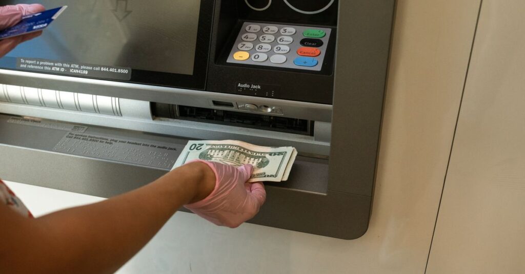 The Boring Giant Just Learned a New Trick A person wearing gloves withdrawing cash from an ATM machine showcasing money handling and hygiene.