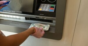 News A person wearing gloves withdrawing cash from an ATM machine showcasing money handling and hygiene.