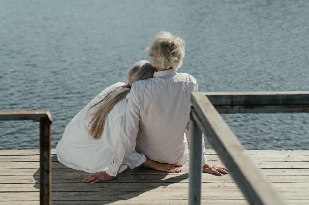 Longevity Science Left the Lab and Moved Into Daily Life A senior couple enjoys a peaceful moment sitting together on a wooden dock by the lake, symbolizing enduring love.