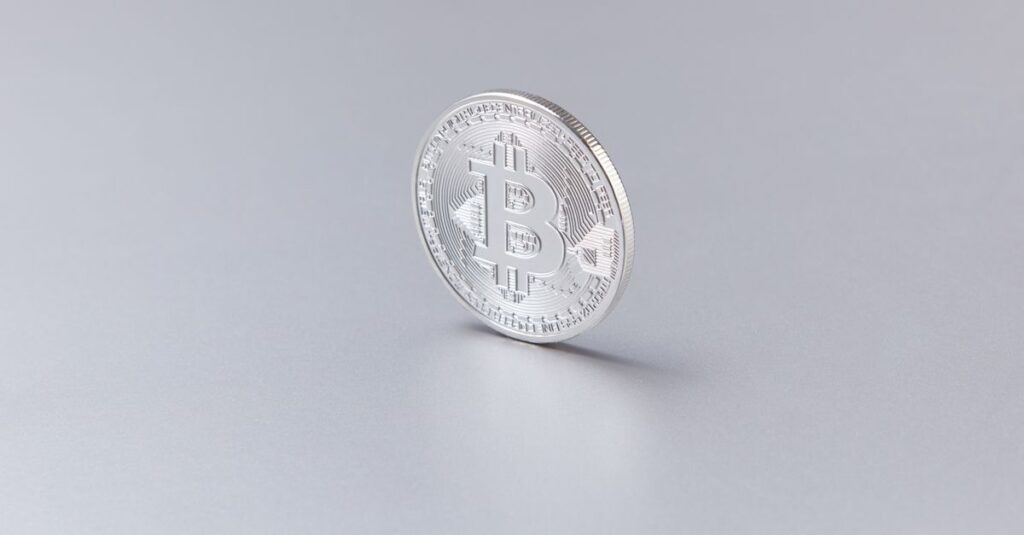 Close-up of a silver Bitcoin coin standing upright against a clean, white background.