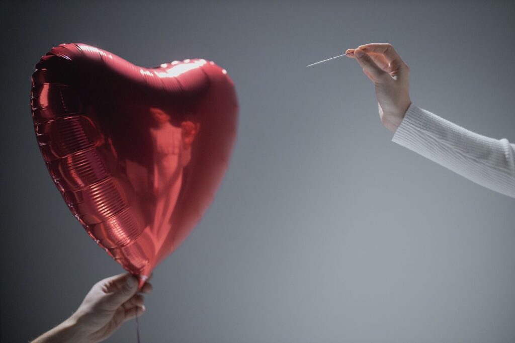 Inflation Fell. Now Watch What Your Savings Do. Close-up of a red heart-shaped balloon being popped by a needle, evoking themes of love and fragility.