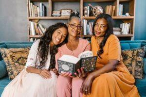 Articles Three women enjoying a relaxed reading session indoors, smiling and bonding.