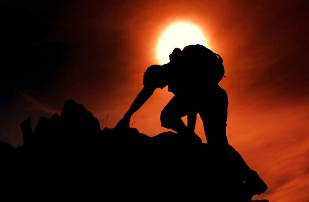 Dramatic silhouette of a climber scaling rocks against a vibrant sunset in Nordland, Norway.