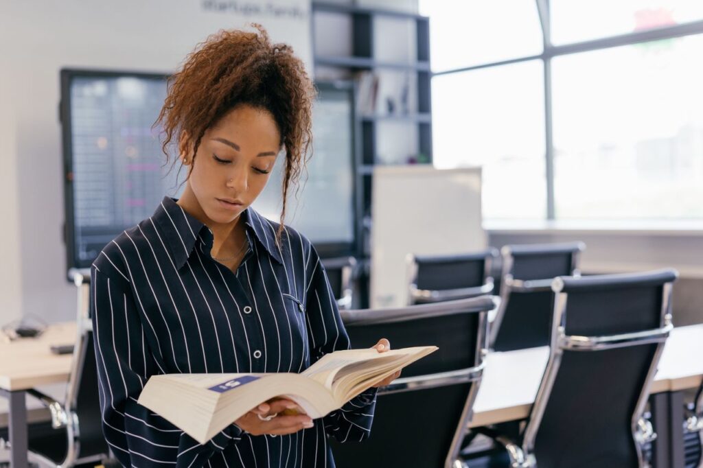 The Asset Markets Cannot Touch A woman reading a book in a conference room with glass windows and office chairs.