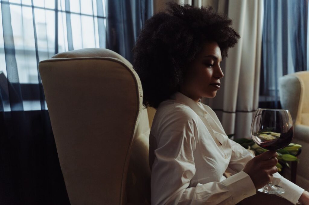 Quiet Luxury Became the Default Aesthetic Woman with afro hair enjoying a glass of red wine indoors, seated in a cozy chair.