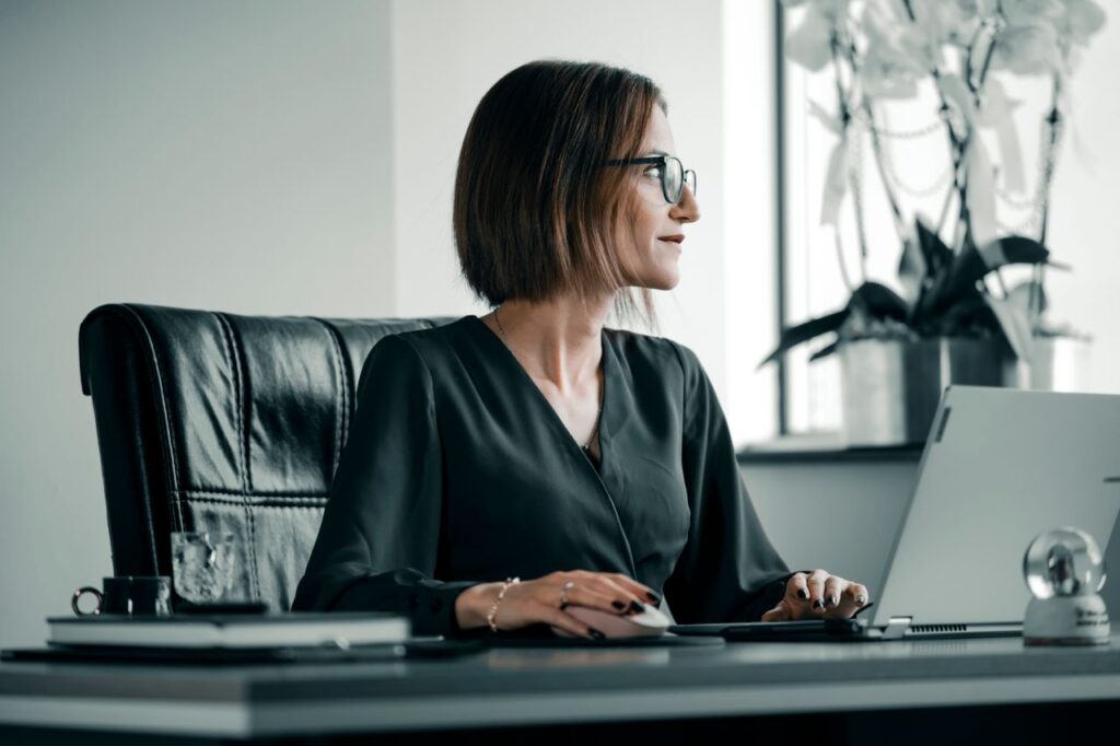 Twenty-Eight Days, And Someone Else Picked Them Adult woman working at office desk with laptop, glasses, and leather chair.
