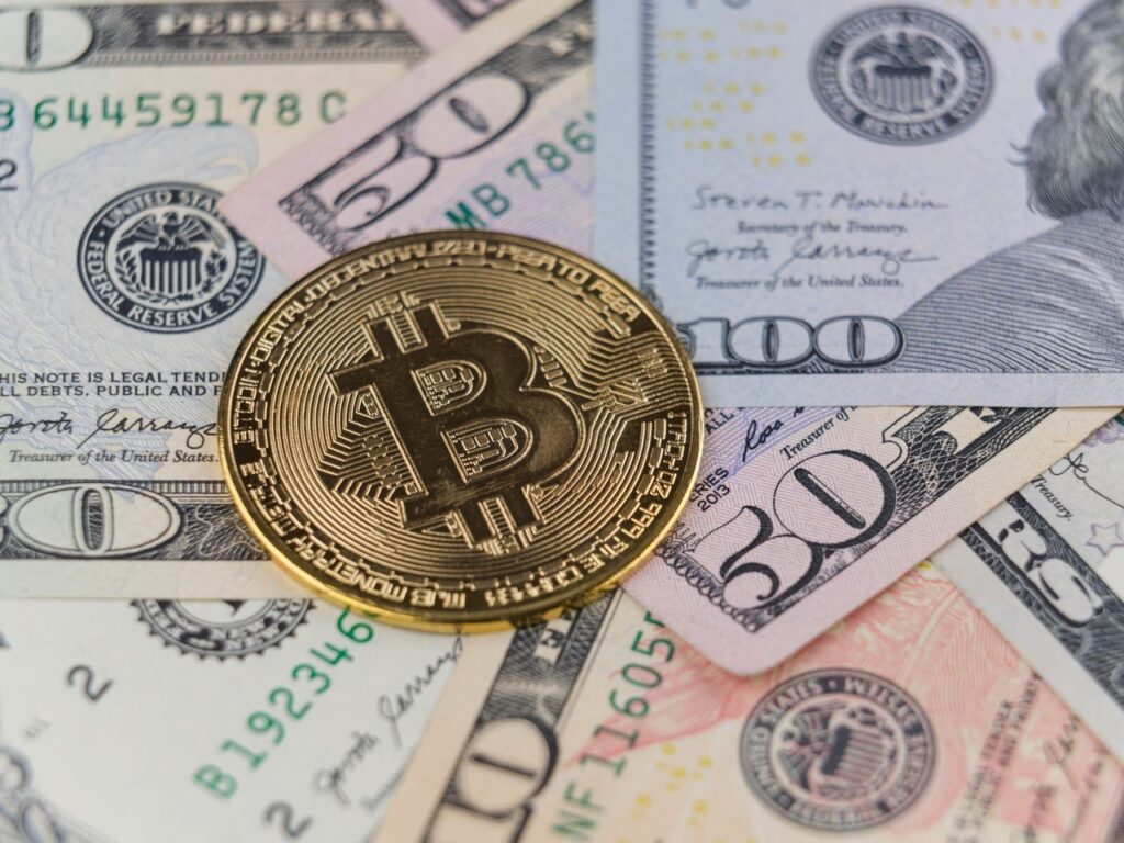 The Speech That Cost Bitcoin Three Per cent in an Afternoon Close-up of a Bitcoin coin on US dollar banknotes, symbolizing cryptocurrency and traditional finance.