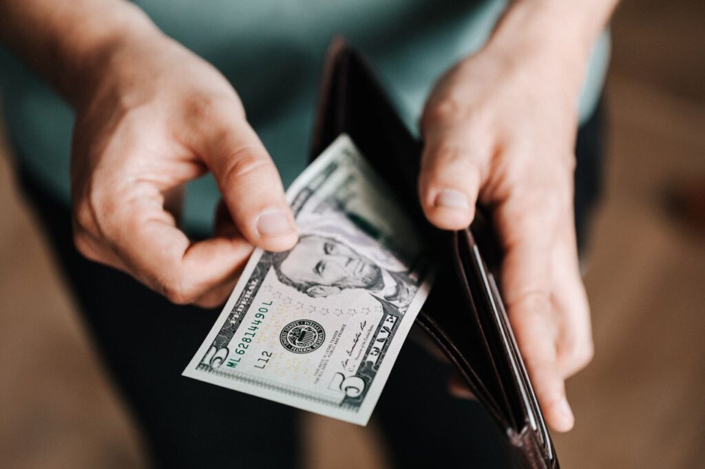Closeup of crop male in casual clothes taking dollars out of wallet while paying in shop