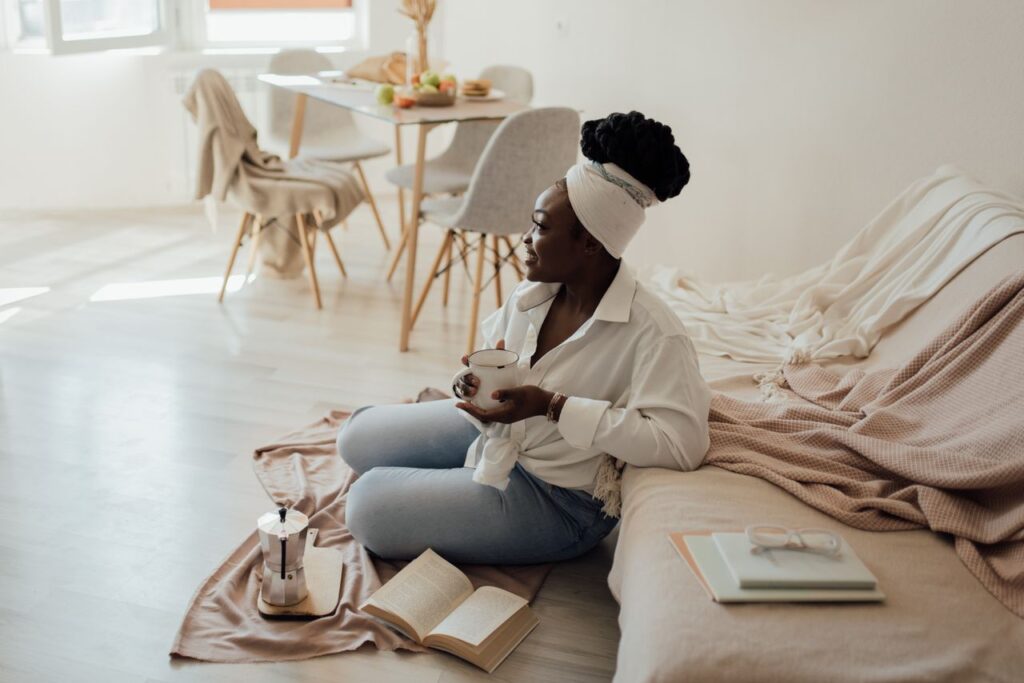 I Don't Want You Rich. I Want You Free. A woman enjoying a cup of coffee in a bright living room setting, surrounded by books and natural light.