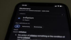 News Close-up of a smartphone screen showing the word inflation defined in a dictionary app.