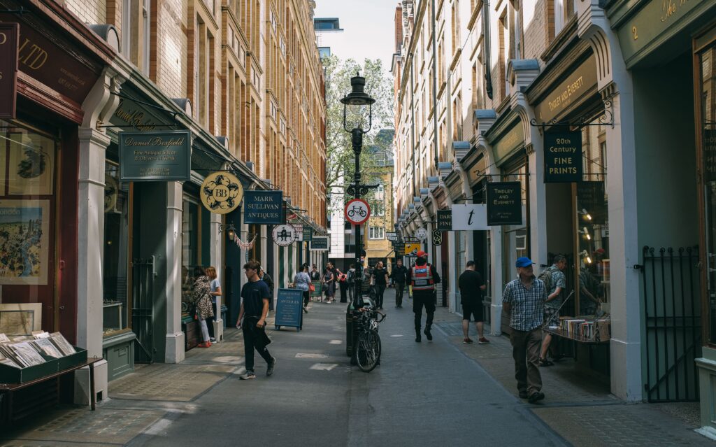 The World Went Shopping in August. Not Equally. Lively London street scene with people shopping in a narrow alley filled with antique shops.
