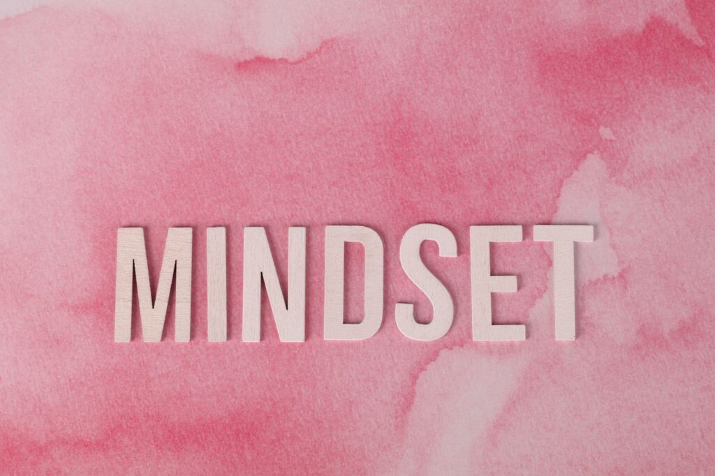 Money Mindset: The Inner Work Nobody Teaches Wooden letters spelling 'MINDSET' on a textured pink background, symbolizing motivation.