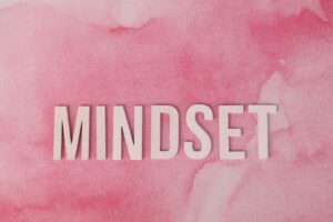 Articles Wooden letters spelling 'MINDSET' on a textured pink background, symbolizing motivation.