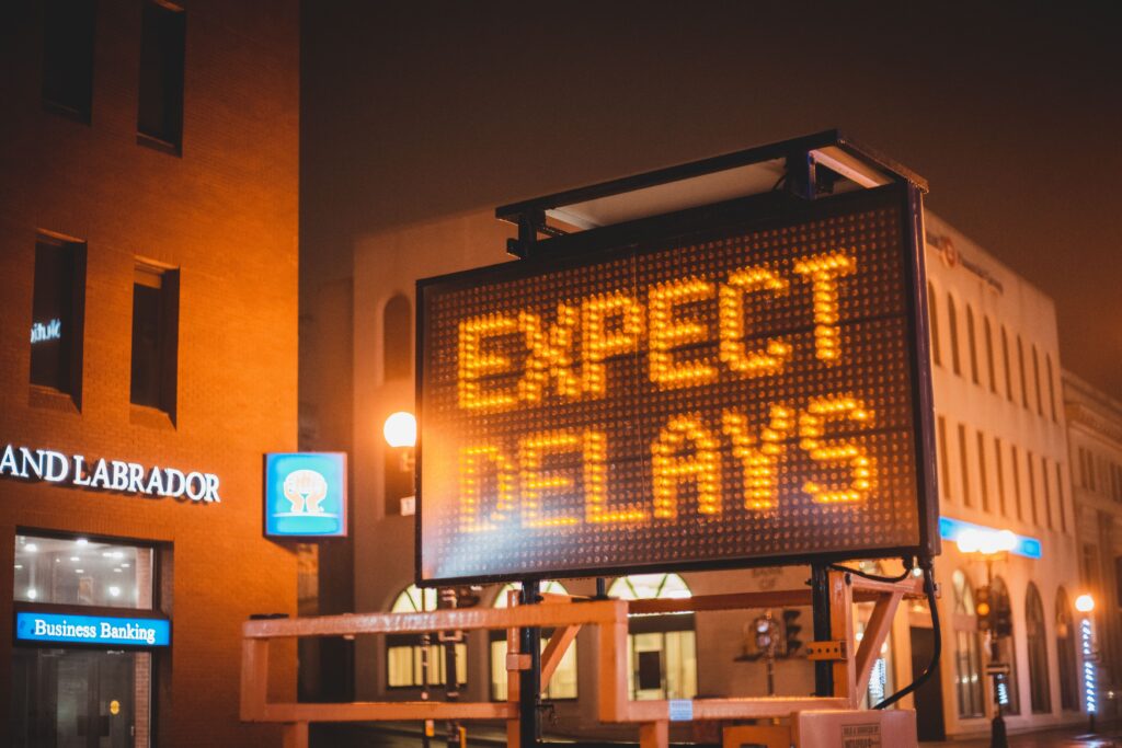 Delayed Gratification Paid Me Back, Slowly Mobile electronic traffic sign with inscription Expect delays placed on road in city street in evening time