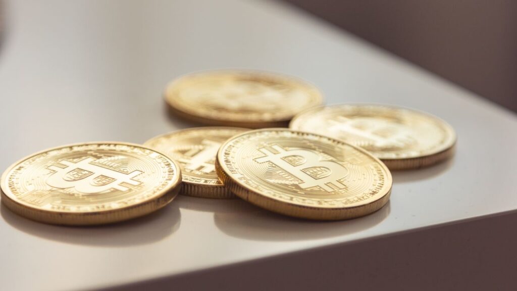 Bitcoin's Rally Met The Rate Debate, And Lost Close-up of shiny gold Bitcoin coins on white surface, symbolizing cryptocurrency wealth.
