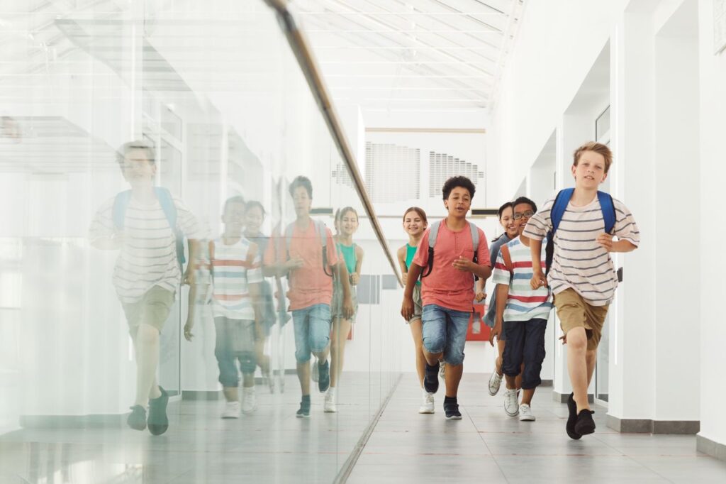The Working Day Does Not End When School Does Group of diverse kids joyfully running in a bright school hallway.