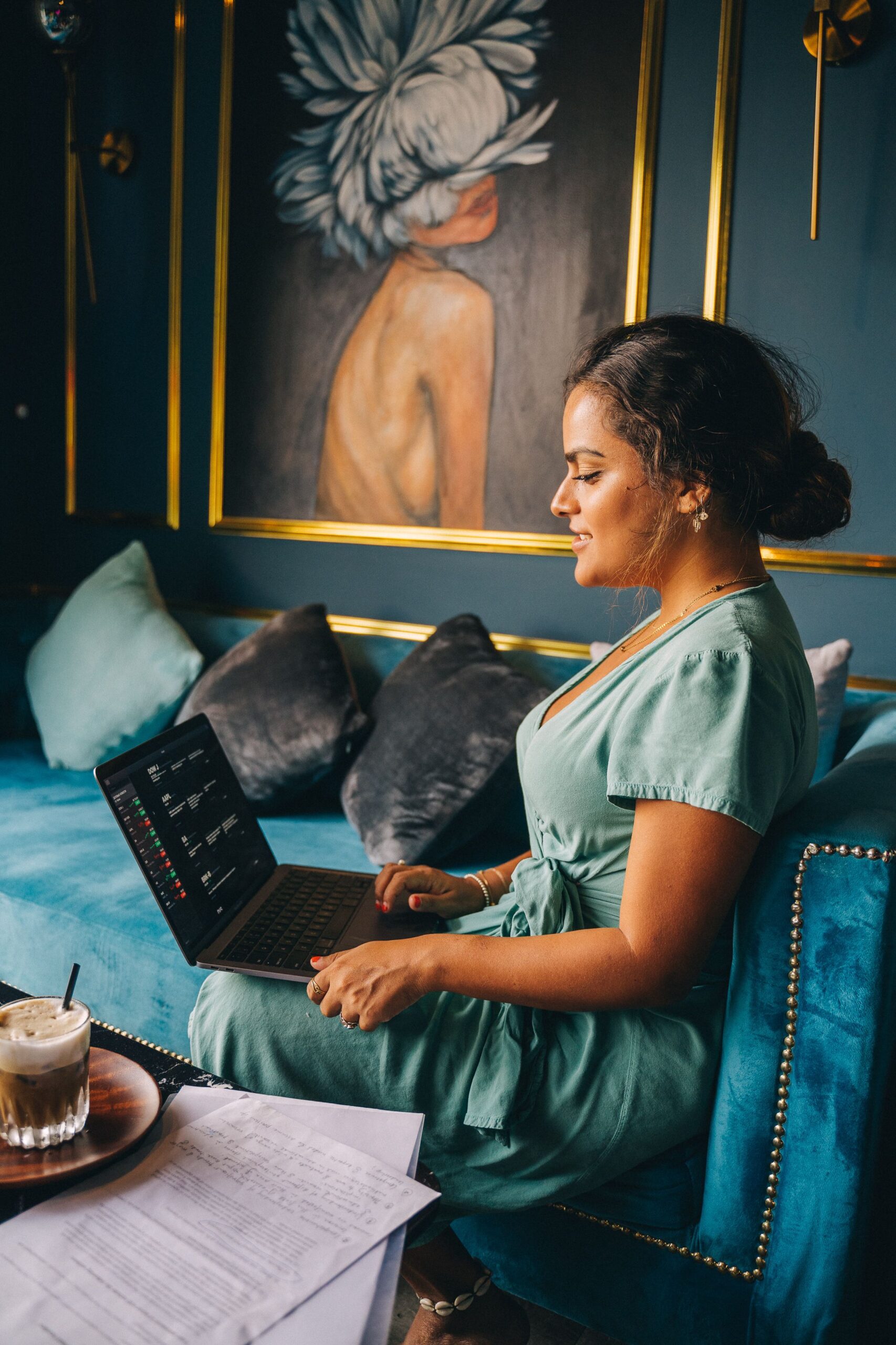 Woman in green dress working on a laptop, seated on a luxurious couch with elegant decor.