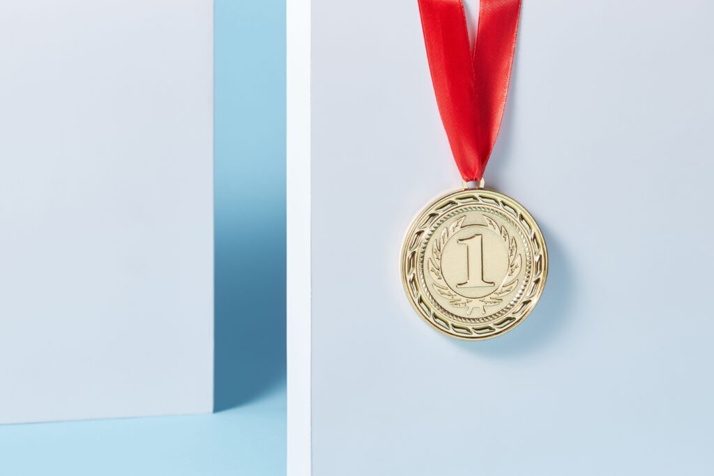 Close-up of a gold medal with a red ribbon hanging against a light blue background.