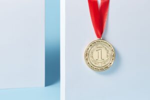 Articles Close-up of a gold medal with a red ribbon hanging against a light blue background.