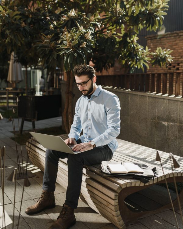 Caucasian man working on laptop outdoors, enjoying remote work environment.